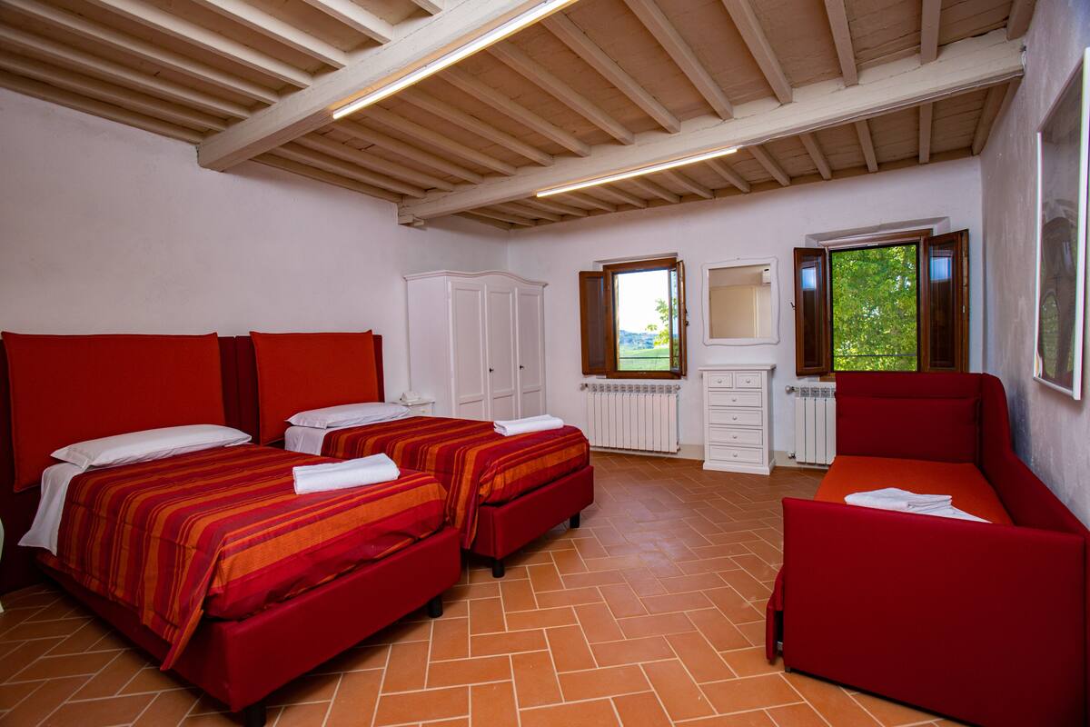 Un dormitorio con dos camas, un sofá rojo y una ventana con vistas al verdor.