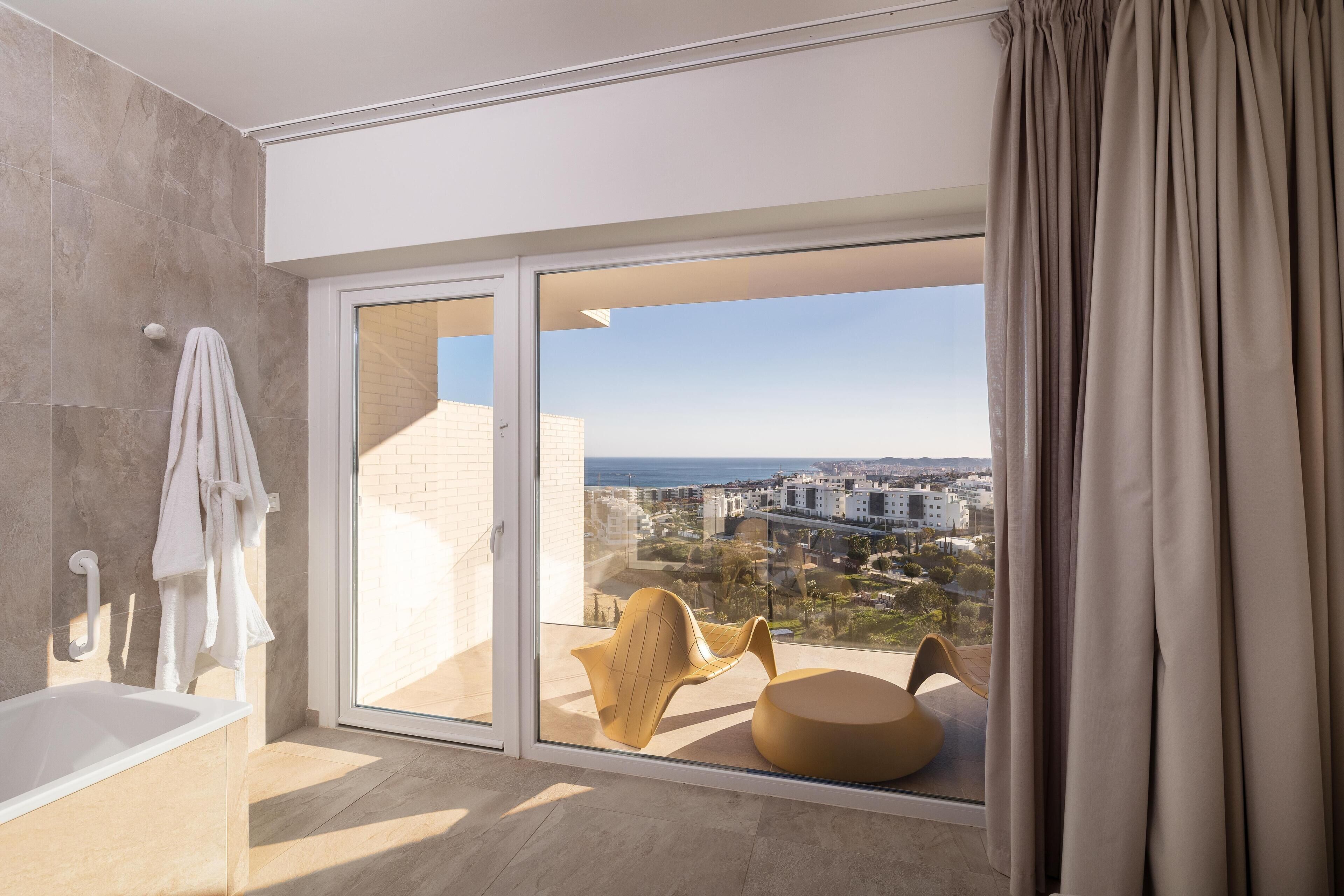 A modern bathroom with a bathtub, a towel rack, and a view of the city through large glass doors.