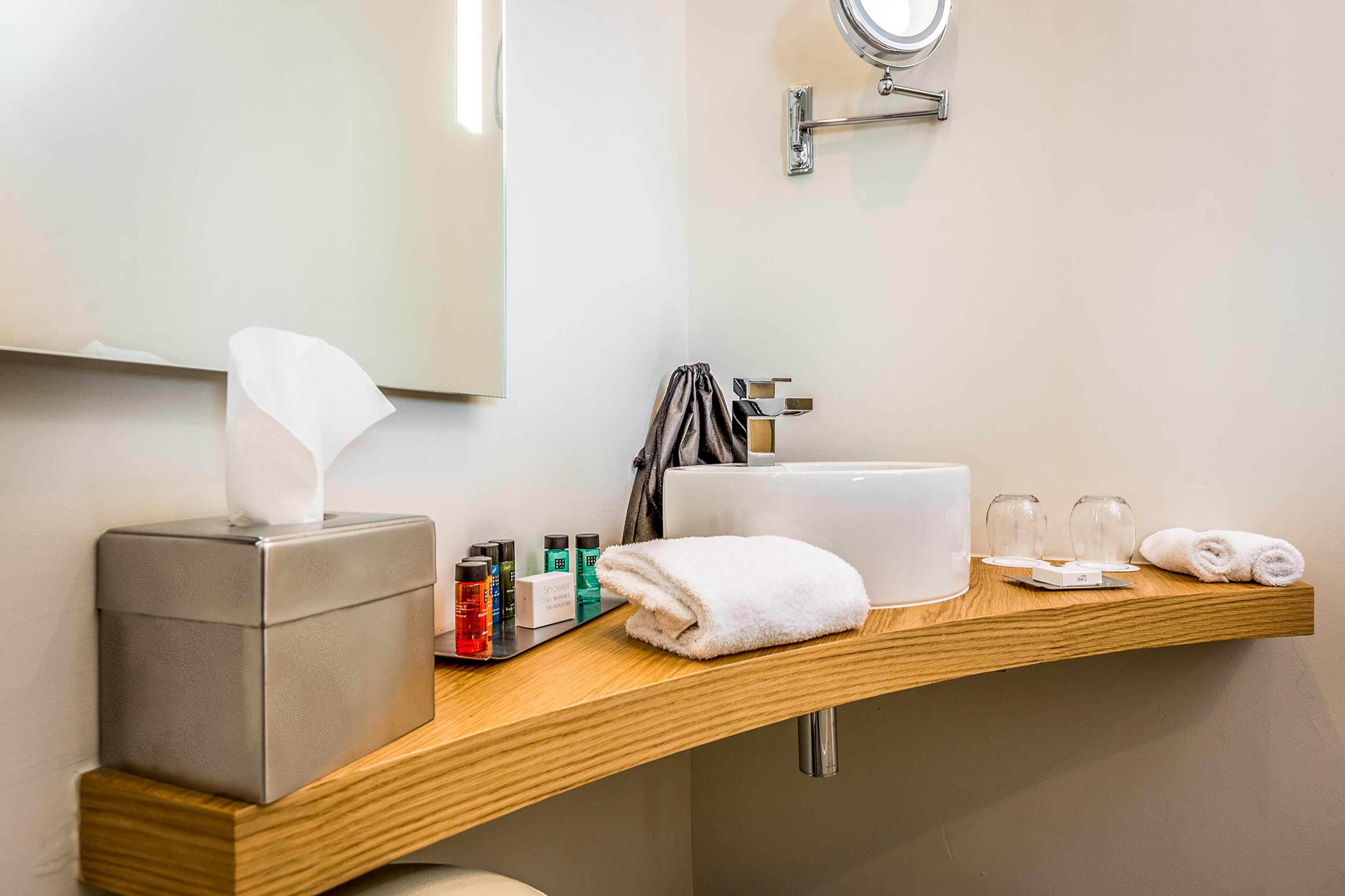 Un baño de hotel con un tocador de madera, una caja de pañuelos, artículos de aseo, una toalla y un lavabo.
