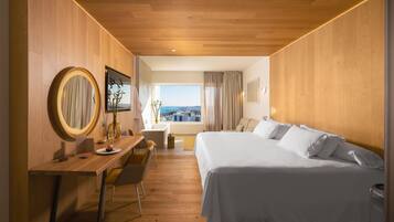 Habitación de hotel con techo de madera, una cama grande, un escritorio con silla, un espejo redondo y vista a la ciudad a través de una ventana.