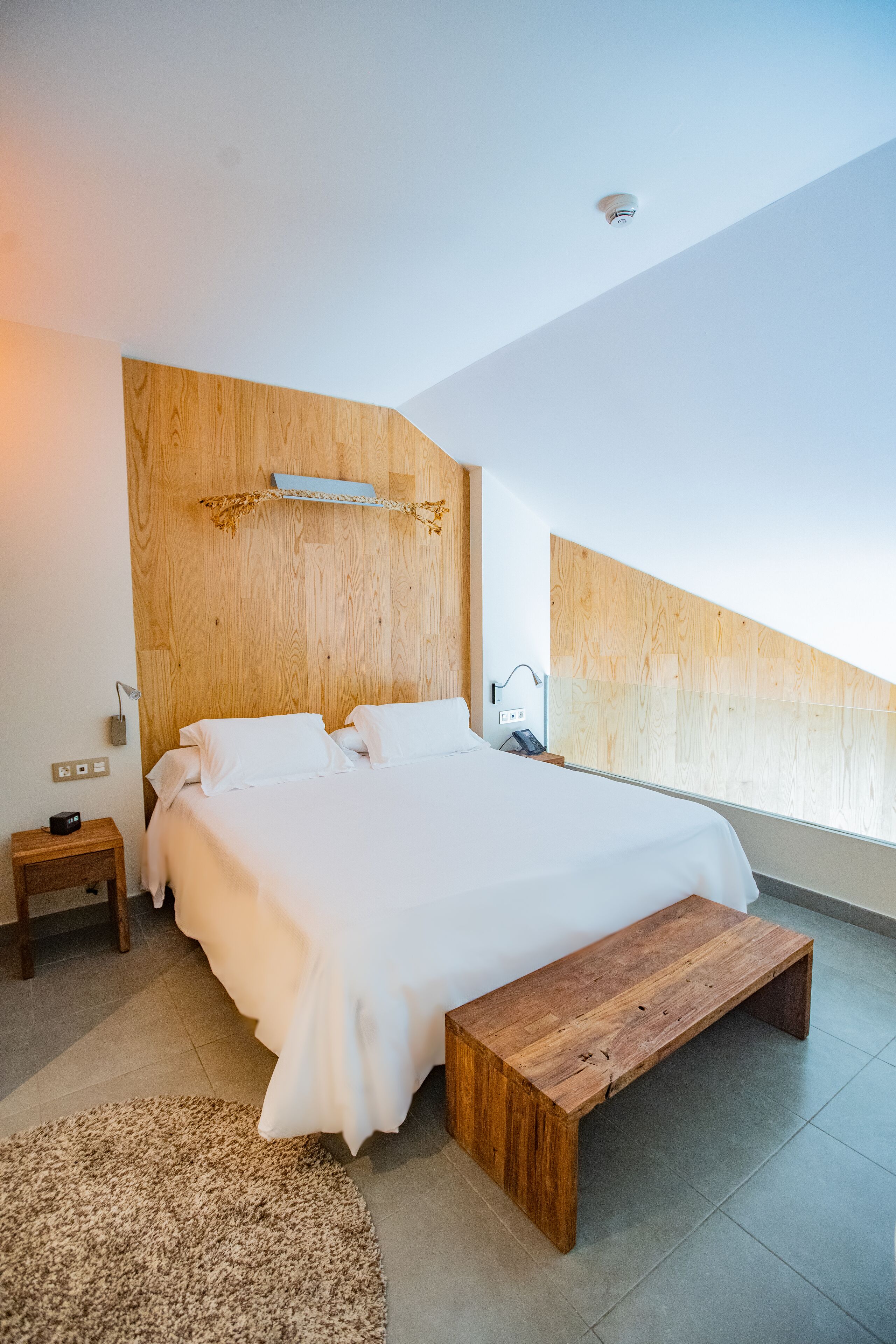 A modern bedroom with a large bed, wooden headboard, bedside tables, and a bench.