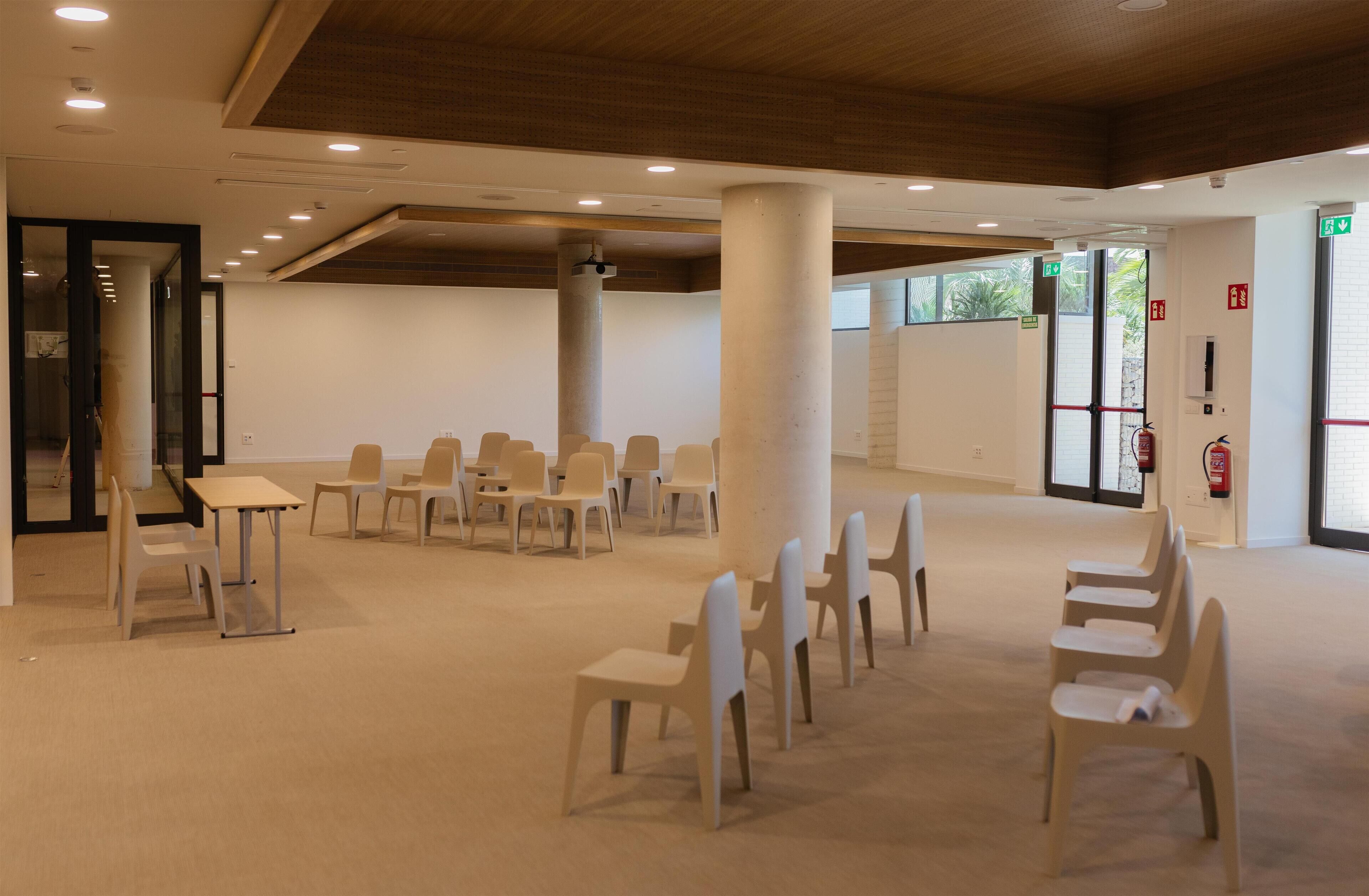 Une pièce spacieuse avec un plafond haut, des chaises blanches disposées en rangées et un sol recouvert de moquette.