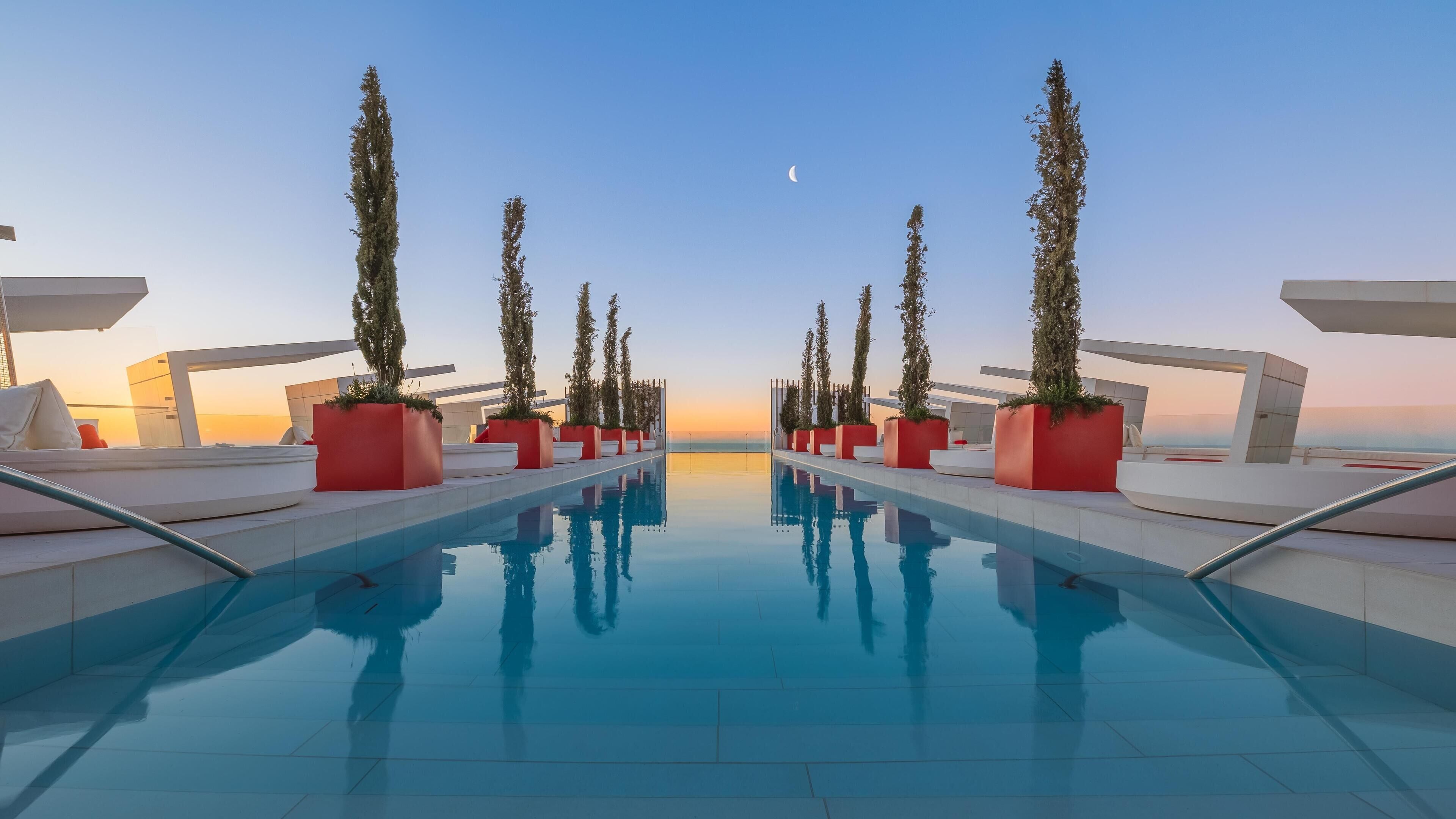 A modern pool area with a clear view of the sunset and a crescent moon in the sky.