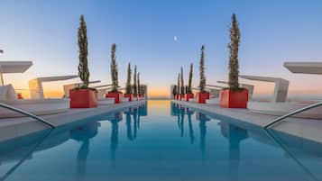 A modern pool area with a clear view of the sunset and a crescent moon in the sky.