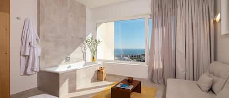 A modern hotel room with a large window, a bathtub, a sofa, and a coffee table.