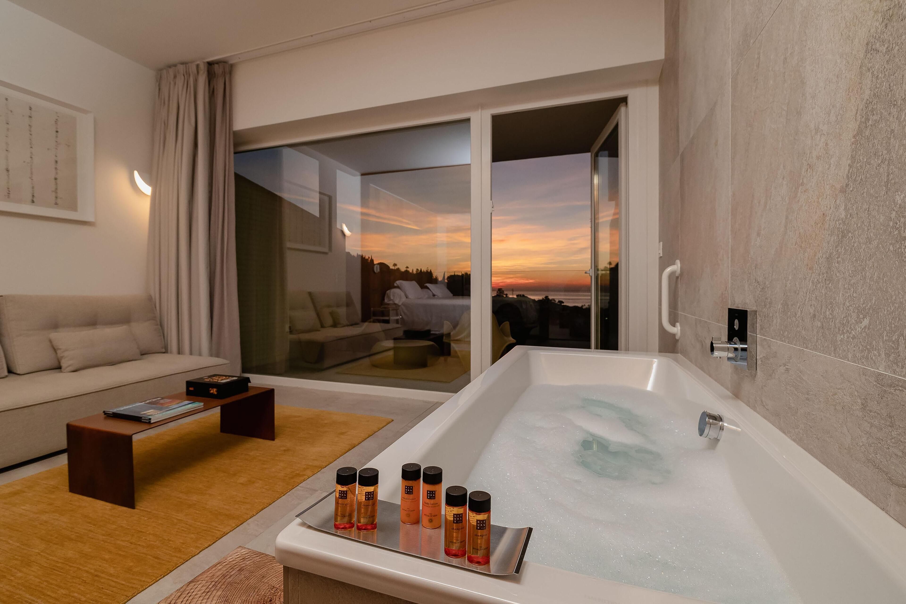 Una habitación de hotel moderna con una bañera grande, un sofá y una mesa de centro.