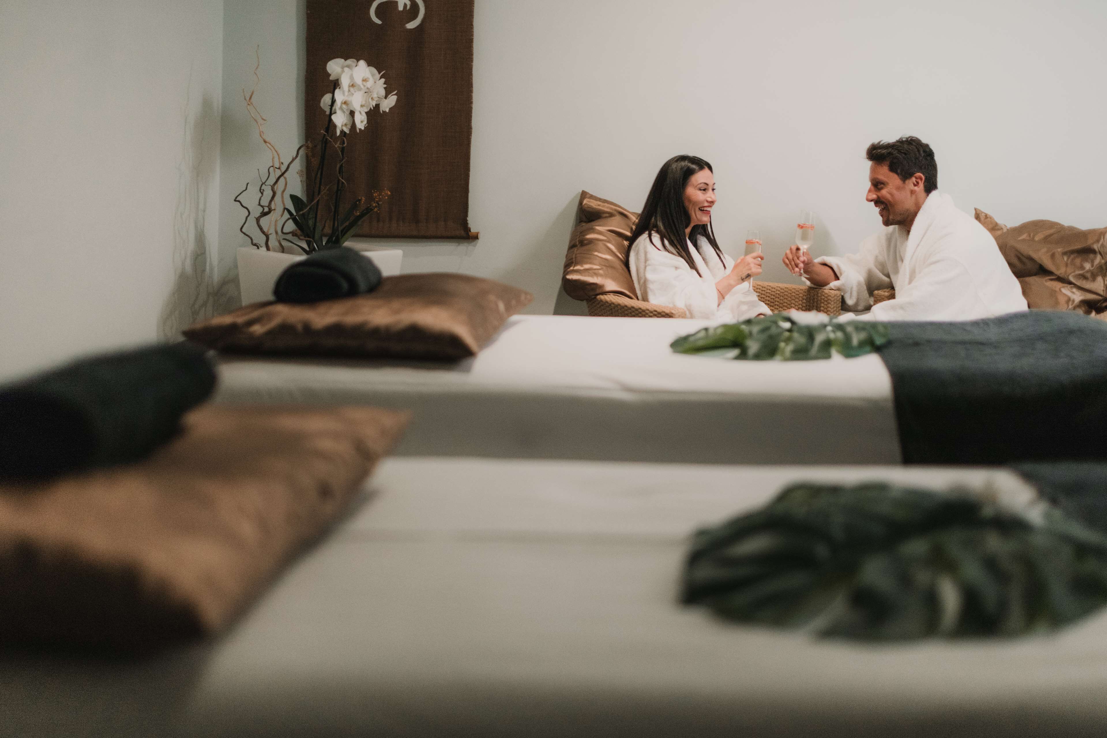 A bedroom with two beds, a potted orchid, and a brown wall hanging.