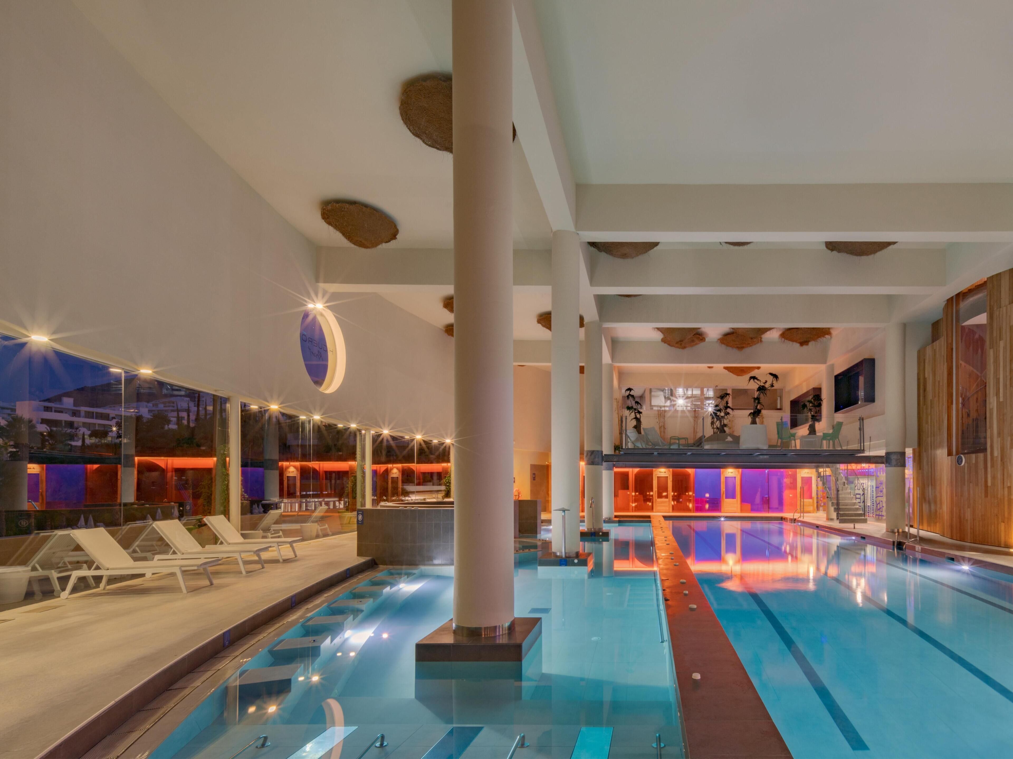 A swimming pool with lounge chairs, a bar area, and a view of the cityscape at dusk.