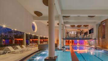 A swimming pool with lounge chairs, a bar area, and a view of the cityscape at dusk.