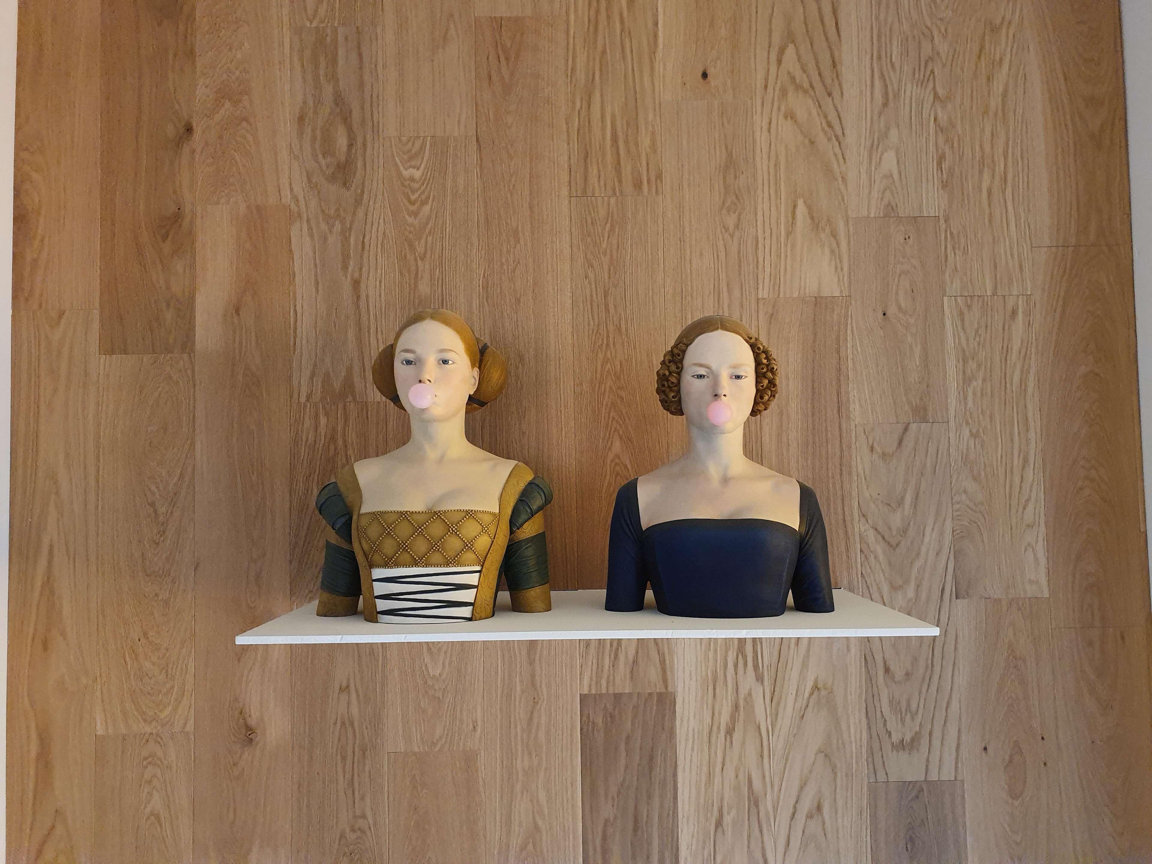 Deux bustes sont posés sur une étagère blanche, adossée à un mur en bois.