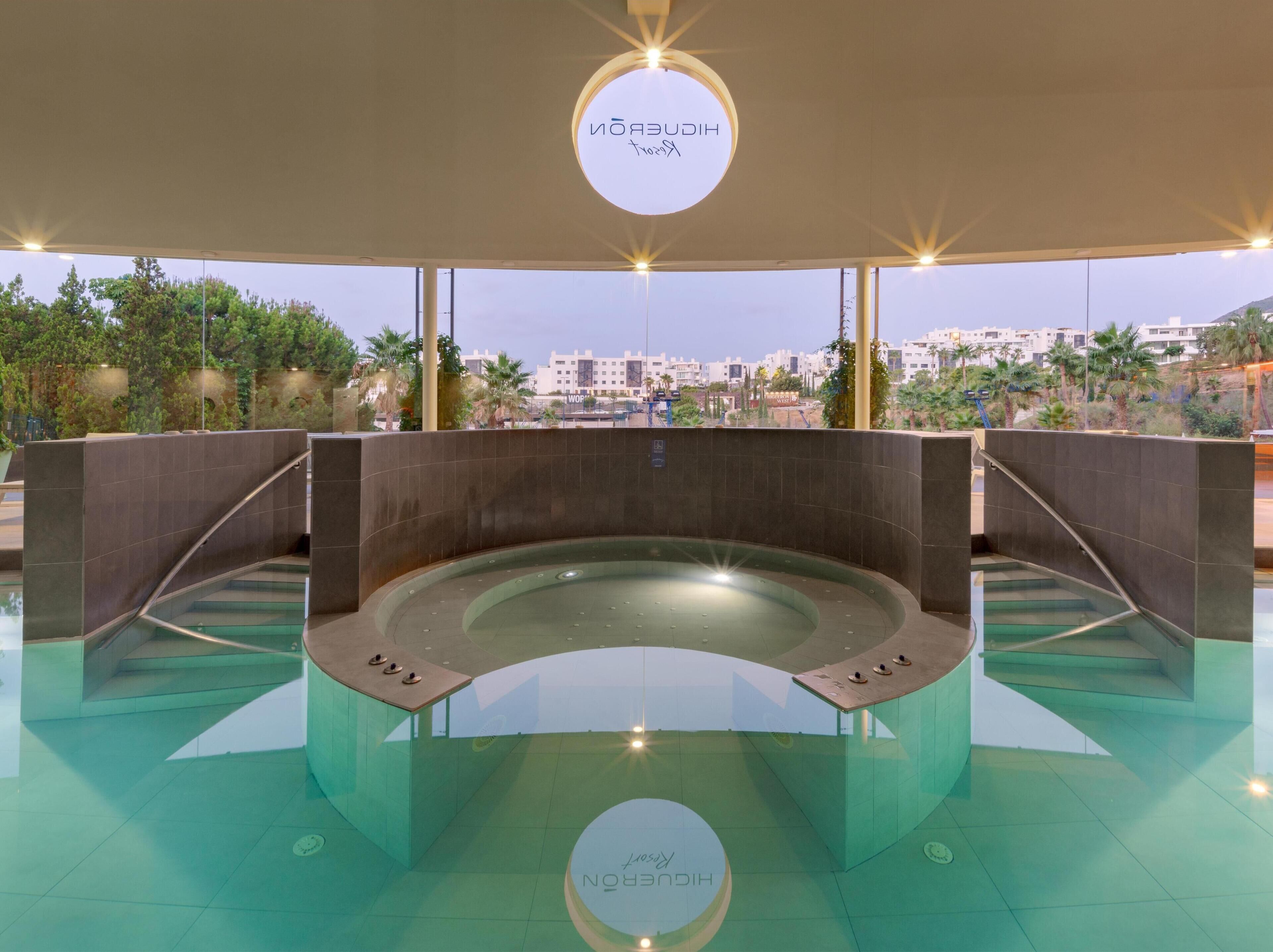 Piscina interna moderna con fondo in vetro, circondata da piastrelle scure e vista sulla città.