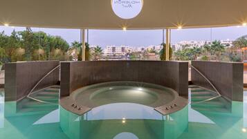 Piscina interna moderna con fondo in vetro, circondata da piastrelle scure e vista sulla città.