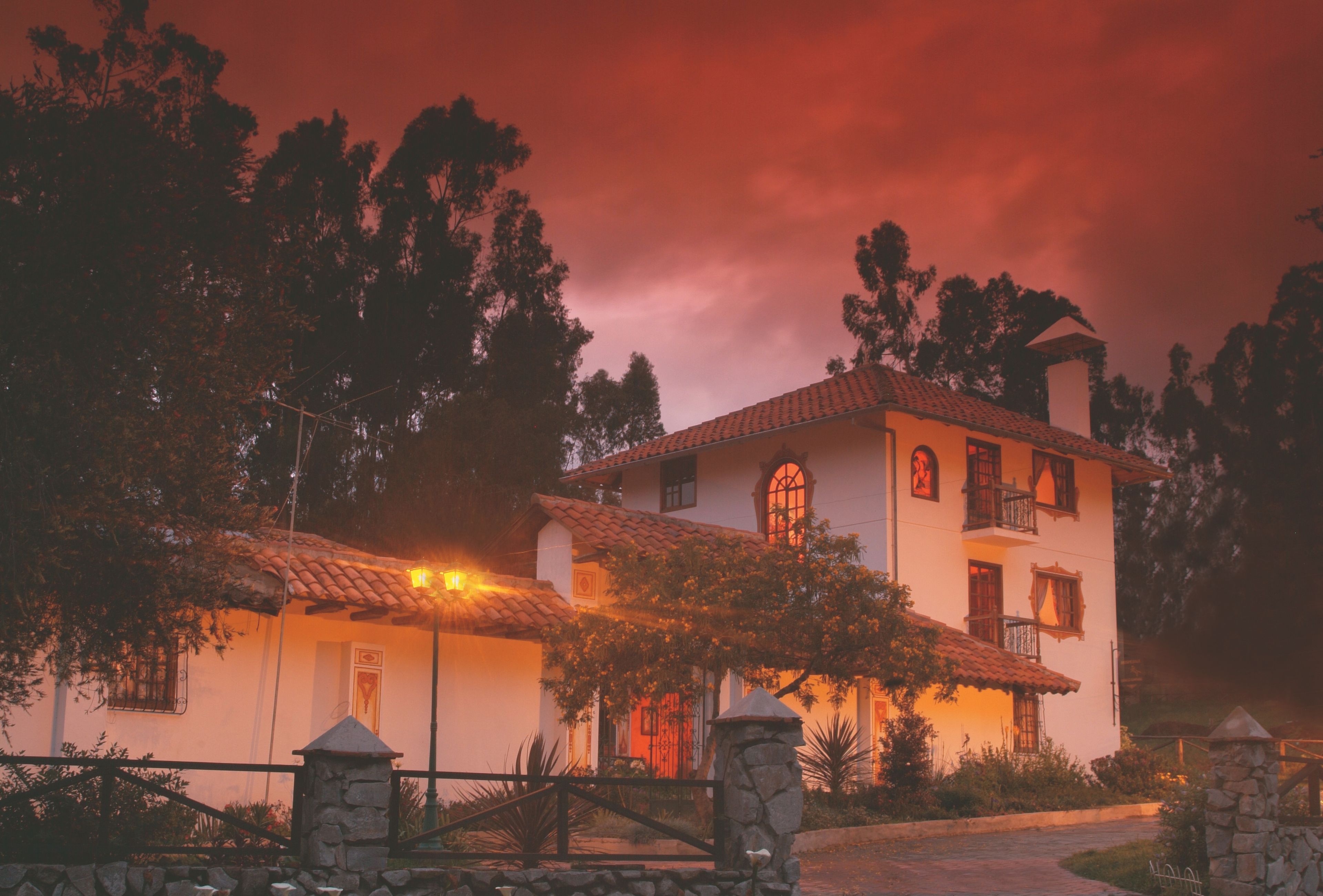 Una casa de dos pisos con techo de tejas, pilares de piedra y un jardín bien cuidado.