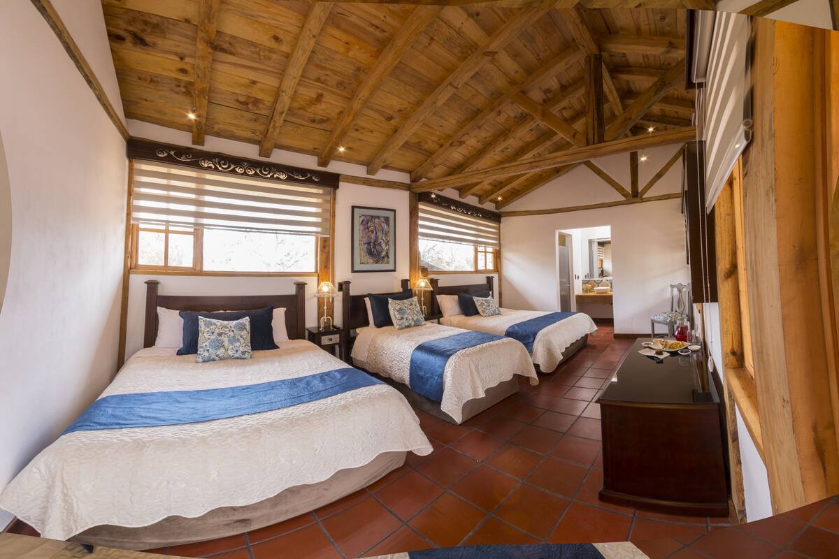 A bedroom with two beds, wooden ceiling beams, and a small desk with a mirror.