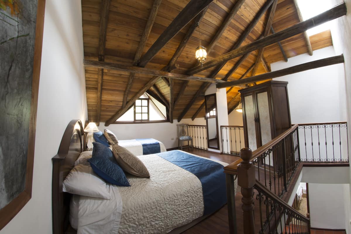 A bedroom with a wooden ceiling, a bed with a white and blue bedspread, and a staircase with a wooden railing.