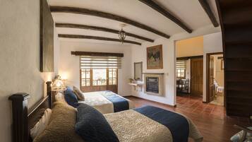 Una habitación con dos camas, vigas de madera en el techo, chimenea y un comedor al fondo.