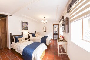 A hotel room with two beds, a small table with a cup and saucer, a mirror, and a window with a view.