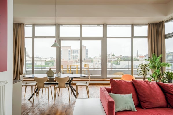 Relax in this stylish living room with a panoramic city view, featuring a comfortable sofa, dining area, and potted plant.