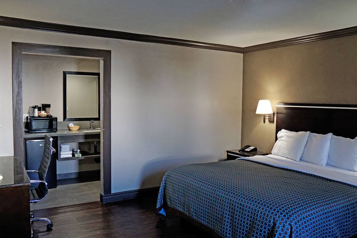 Una habitación de hotel con una cama, un escritorio con lámpara, un microondas y una pequeña kitchenette.