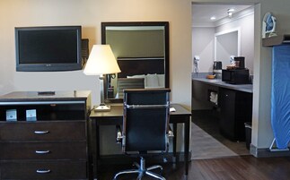 Habitación de hotel con escritorio, silla, televisión, lámpara y una zona de kitchenette.