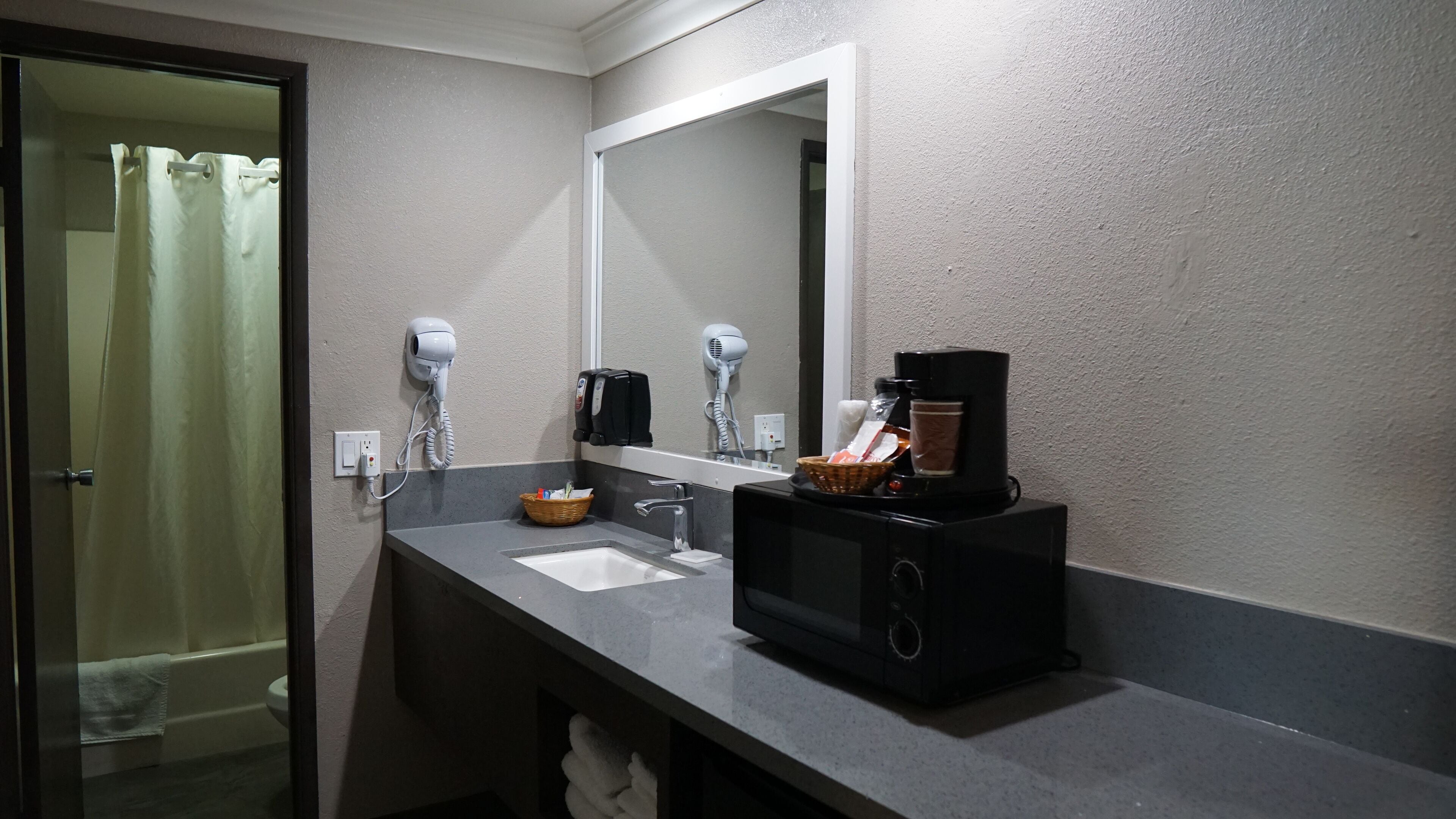 Une salle de bain équipée d’un lavabo, de deux sèche-cheveux, d’une machine à café et d’un panier contenant des articles de toilette.