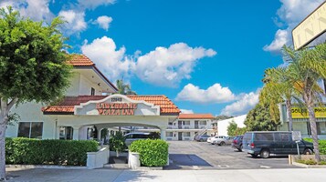 Hawthorne Plaza Inn with a clear blue sky, a parking lot, and a building with a red-tiled roof.
