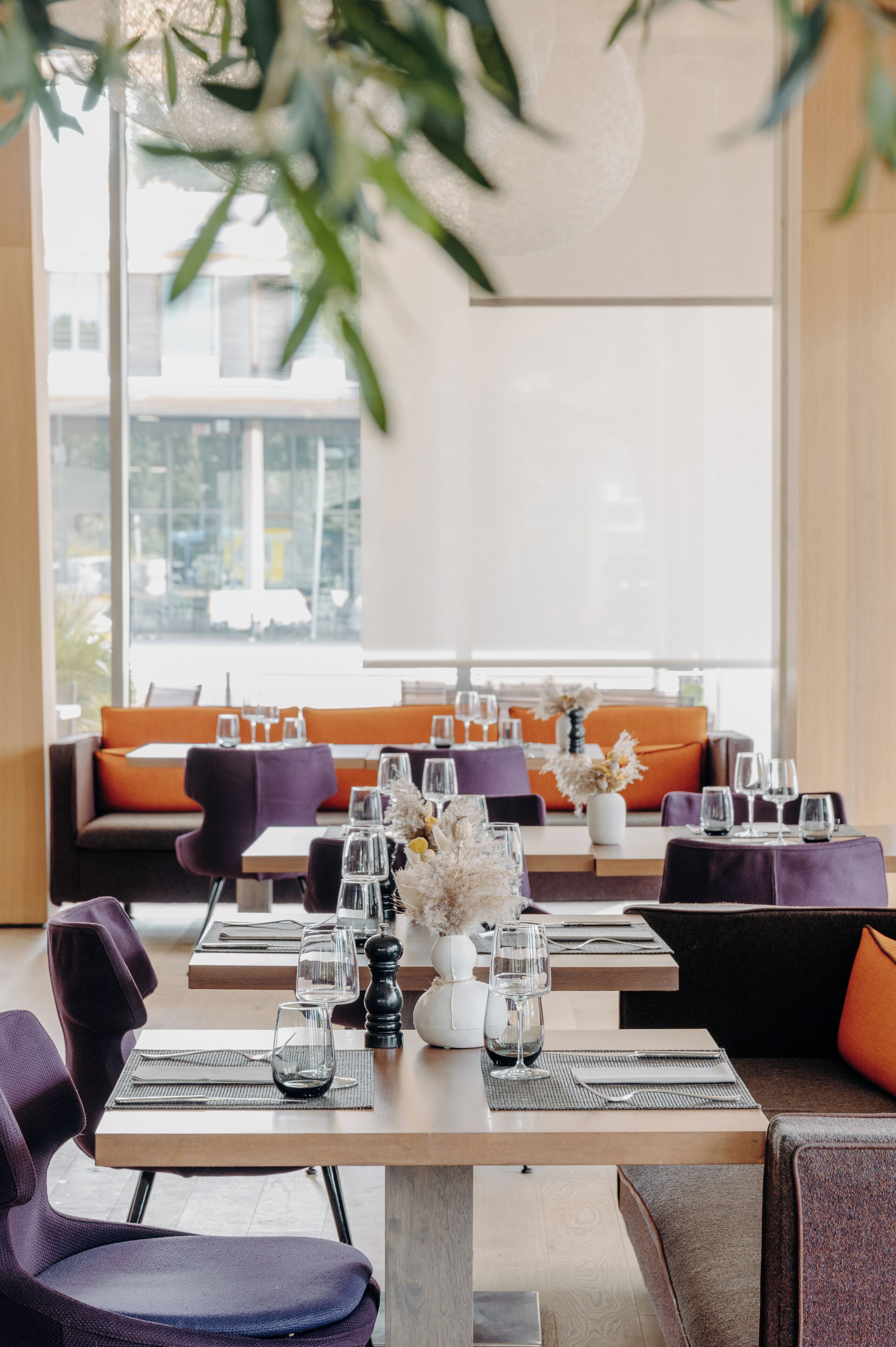 Un restaurante moderno con una larga mesa dispuesta para comer, asientos acolchados y un amplio ventanal con vistas a la ciudad.