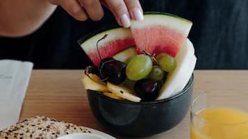 Une table en bois dressée pour le petit-déjeuner, avec des croissants, un saladier de fruits, un verre de jus d’orange et un petit ramequin de beurre.