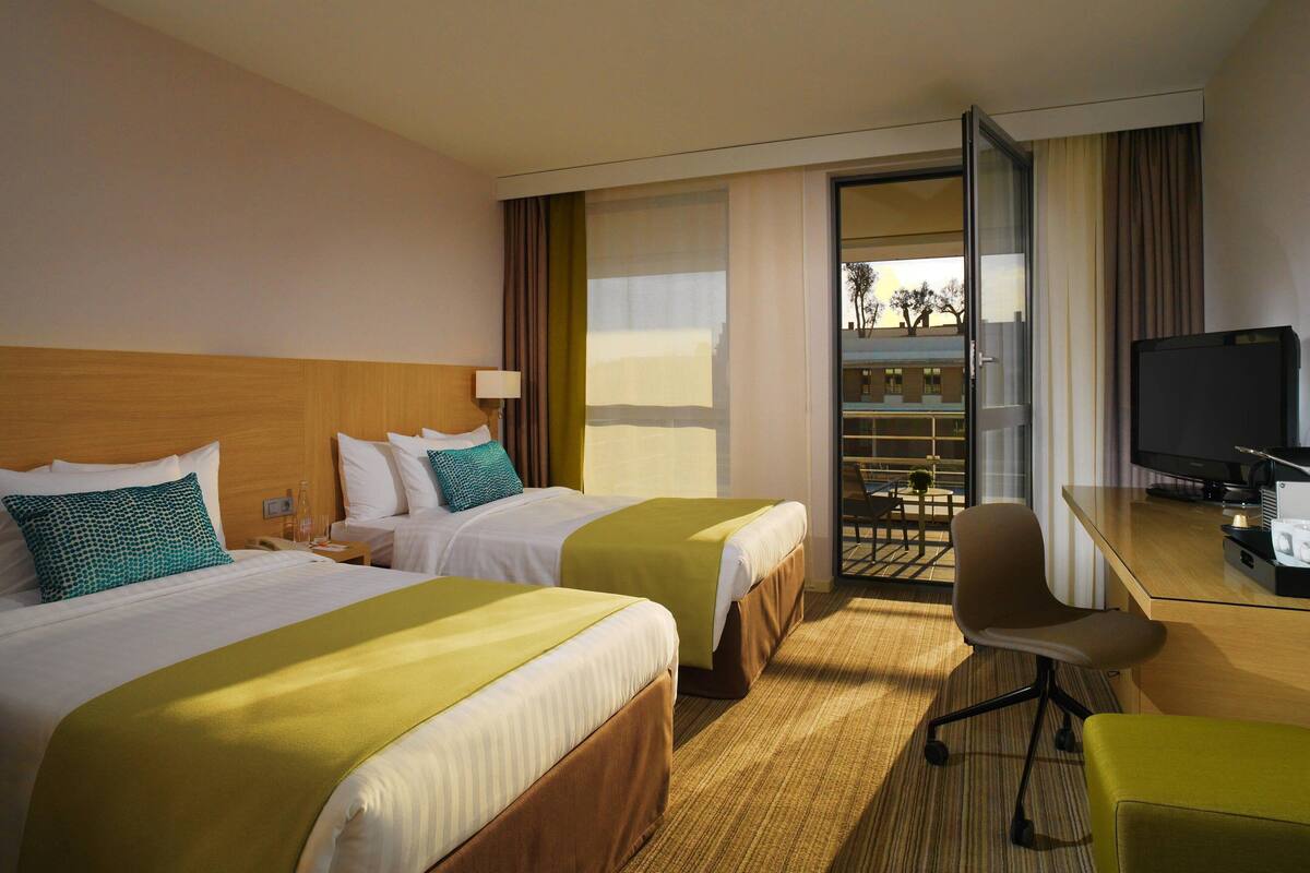 Ein Hotelzimmer mit zwei Betten, einem Schreibtisch mit Computer und einem Fernseher.