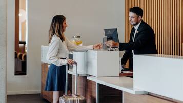 A reception desk with a modern design, a woman with a suitcase, and a man working at the desk.
