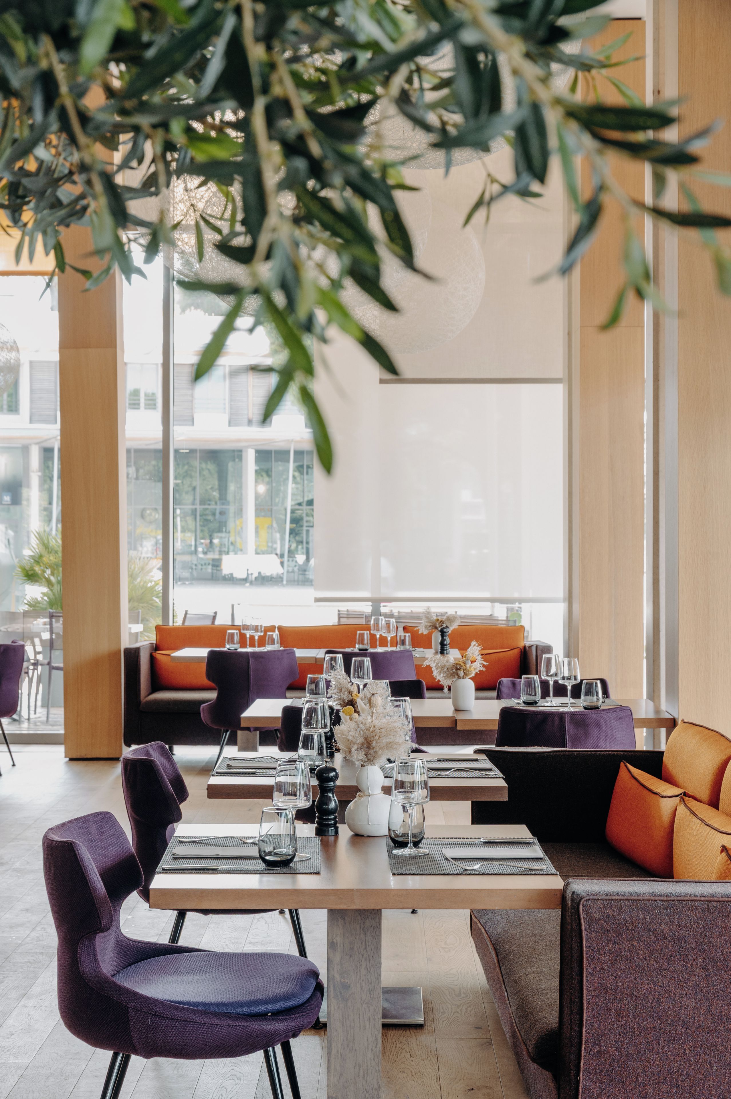 Un espace de restauration moderne avec des tables préparées pour deux personnes, agrémenté d’un mélange de sièges violets et orange.