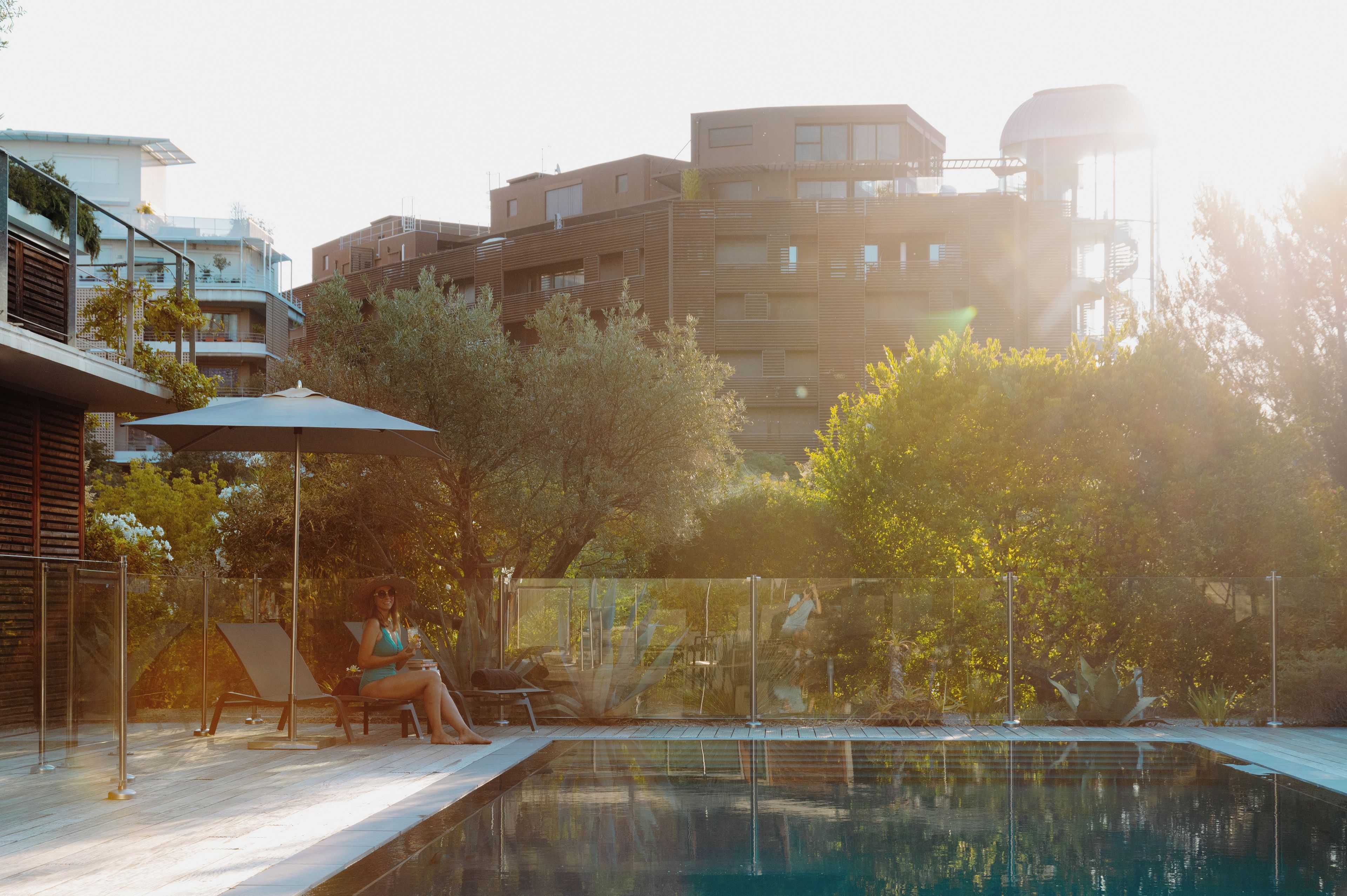 A swimming pool with a lounge area, surrounded by trees and modern buildings.