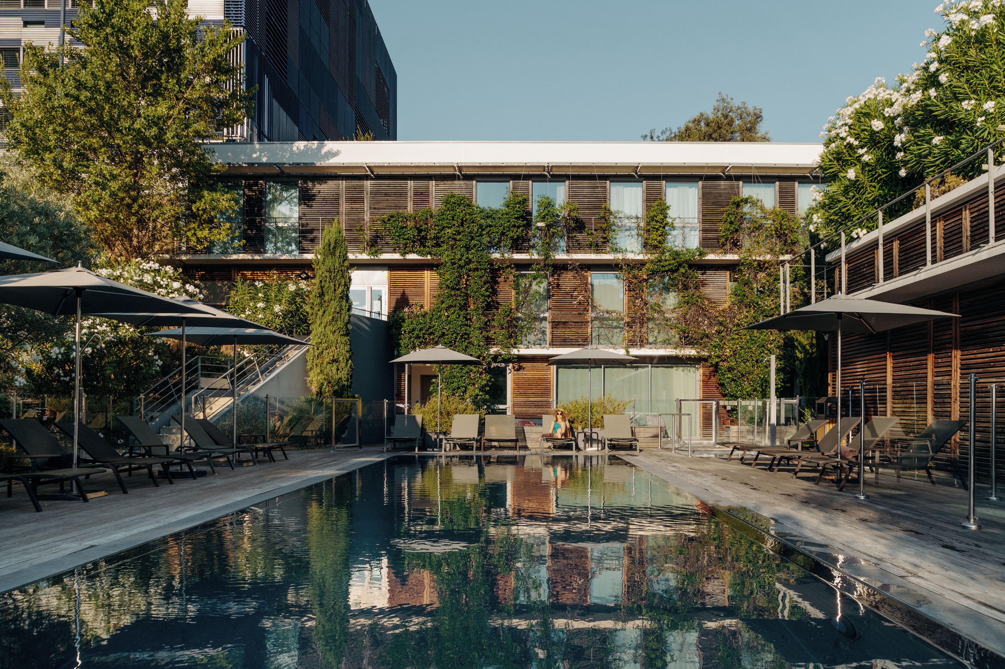 A pool area with lounge chairs and umbrellas, surrounded by buildings with wooden and glass facades.