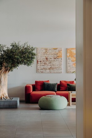 Un salon moderne avec un canapé rouge, un grand arbre et des œuvres d’art abstrait accrochées au mur.