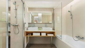 Un baño moderno con cabina de ducha de vidrio, dos lavamanos, un espejo y una bañera.