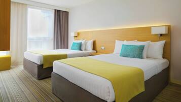 Une chambre d’hôtel avec deux lits, chacun doté d’une tête de lit, une fenêtre avec des rideaux et un sol recouvert de moquette.