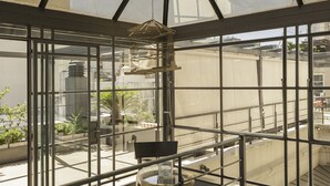 A high-rise building with a glass facade, a balcony with a chair, and a view of the cityscape.