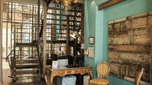 A room with a staircase, a chandelier, a desk, and two chairs.