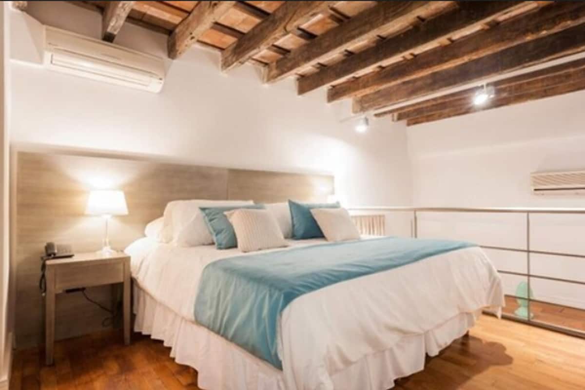 A bedroom with a bed, bedside table, and a wooden ceiling structure.