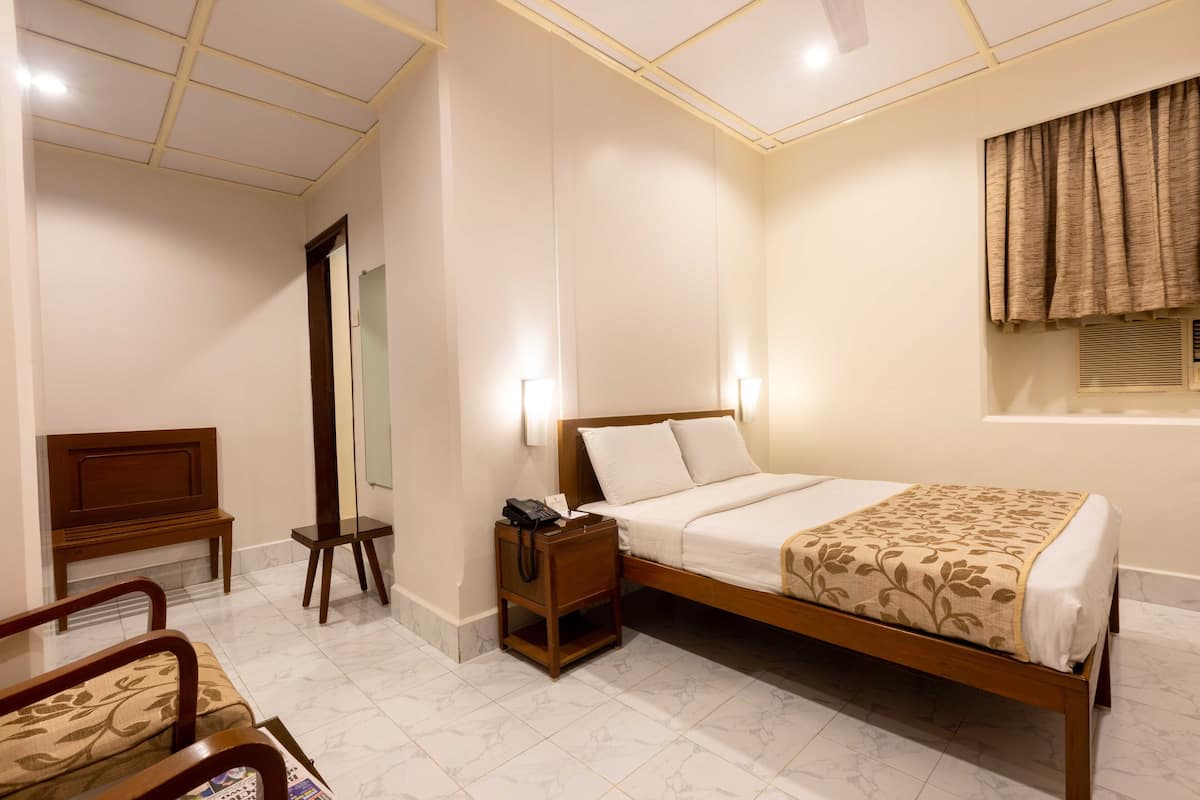 Una habitación de hotel con una cama de madera, una mesita de noche con lámpara, una silla y un espejo grande.