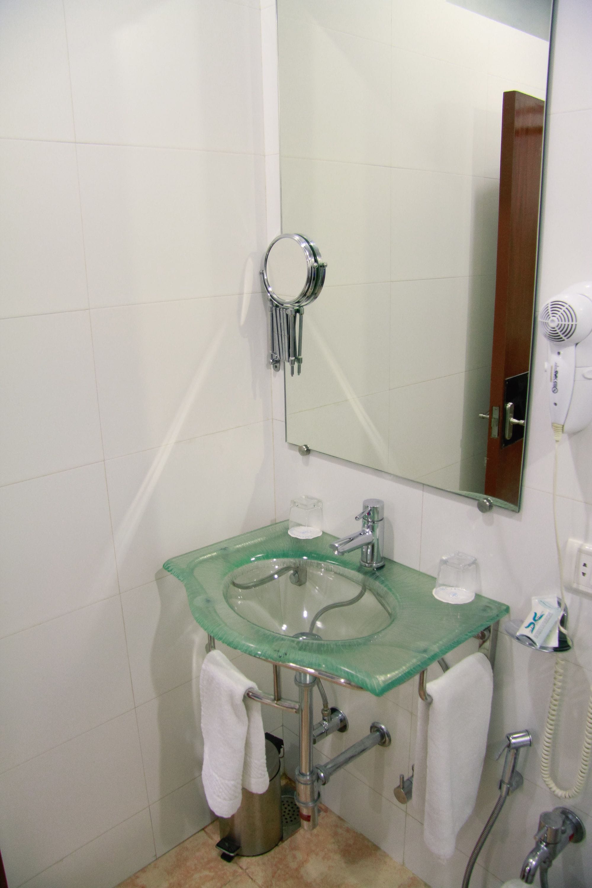 A bathroom with a glass sink, a mirror, a hairdryer, and a towel rack.