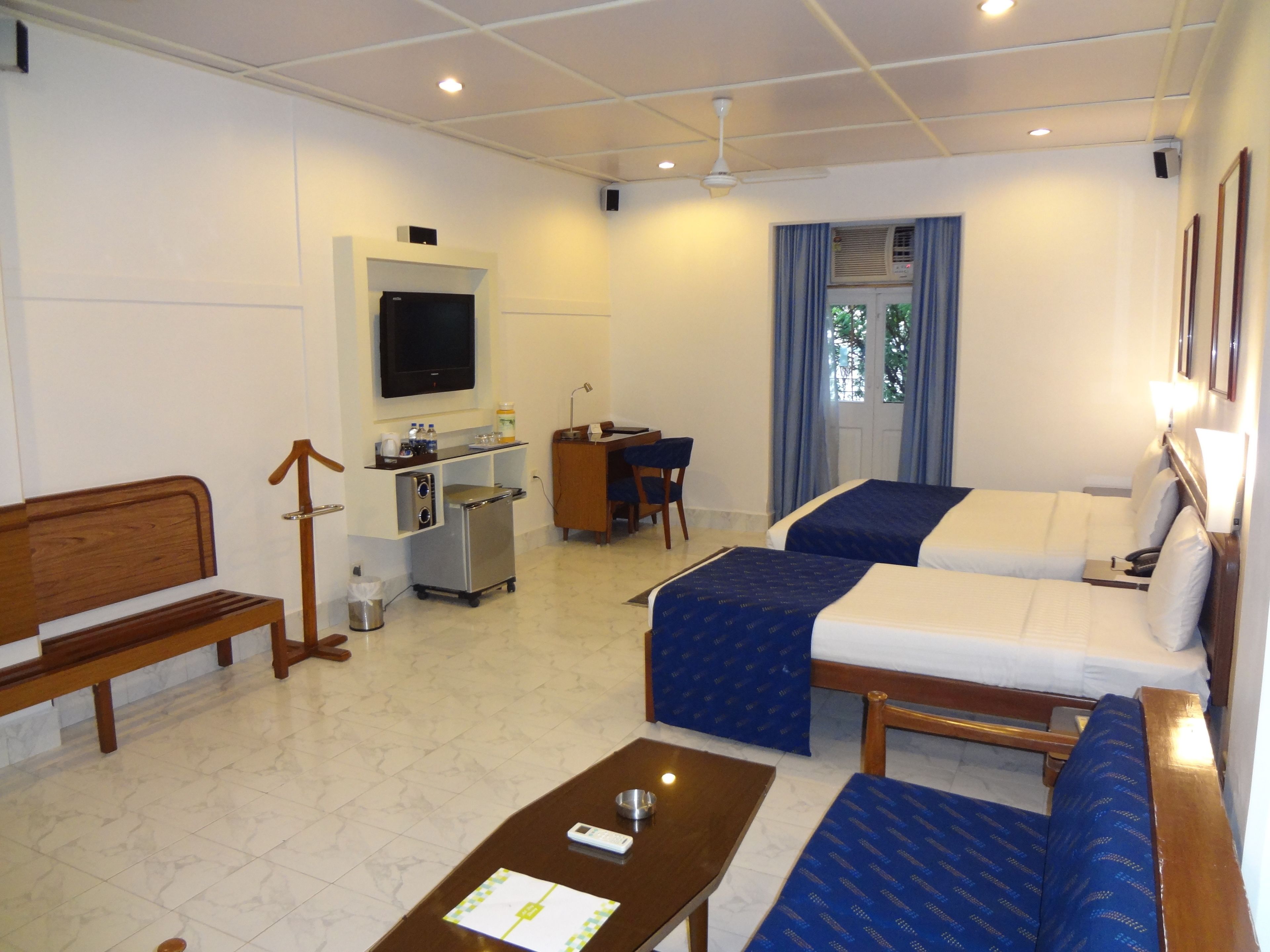 A hotel room with two beds, a desk, a television, and a small kitchenette.