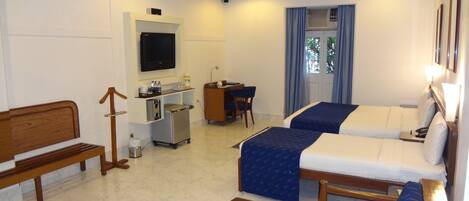 A hotel room with two beds, a desk, a television, and a small kitchenette.