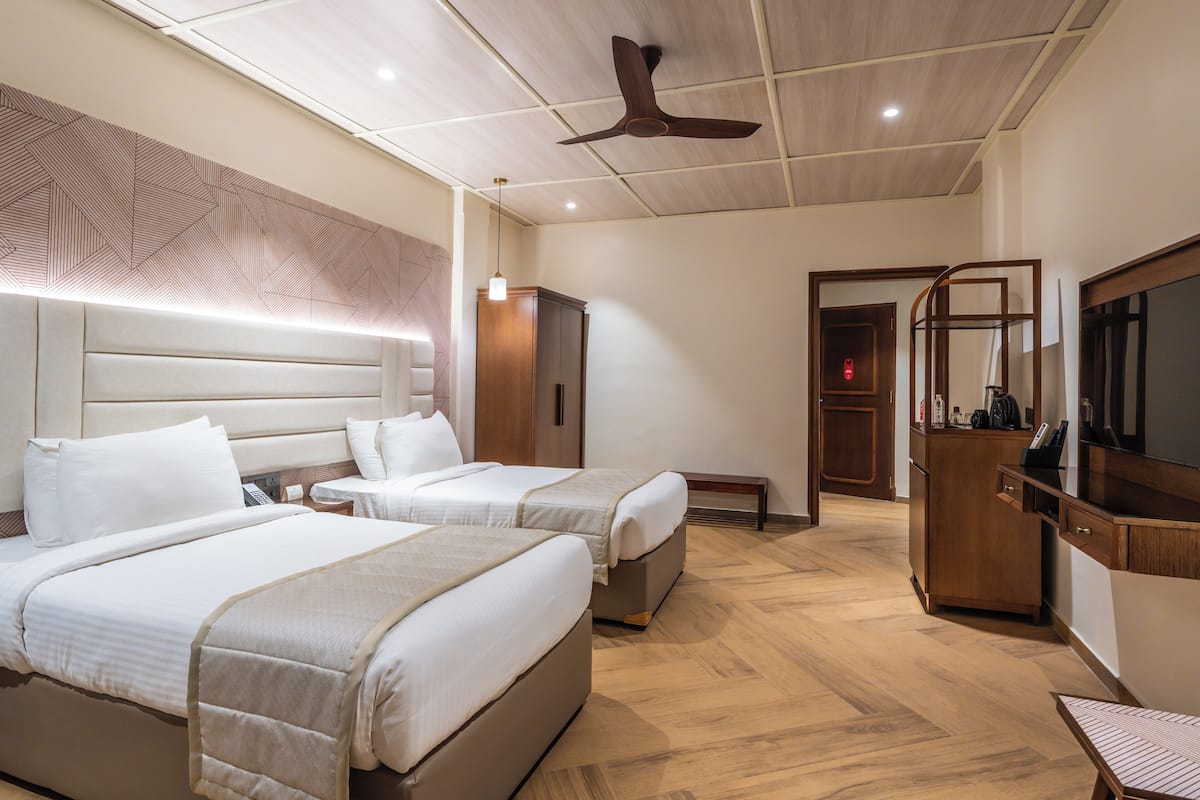 Habitación de hotel con dos camas, ventilador de techo, armario, banco y televisor.