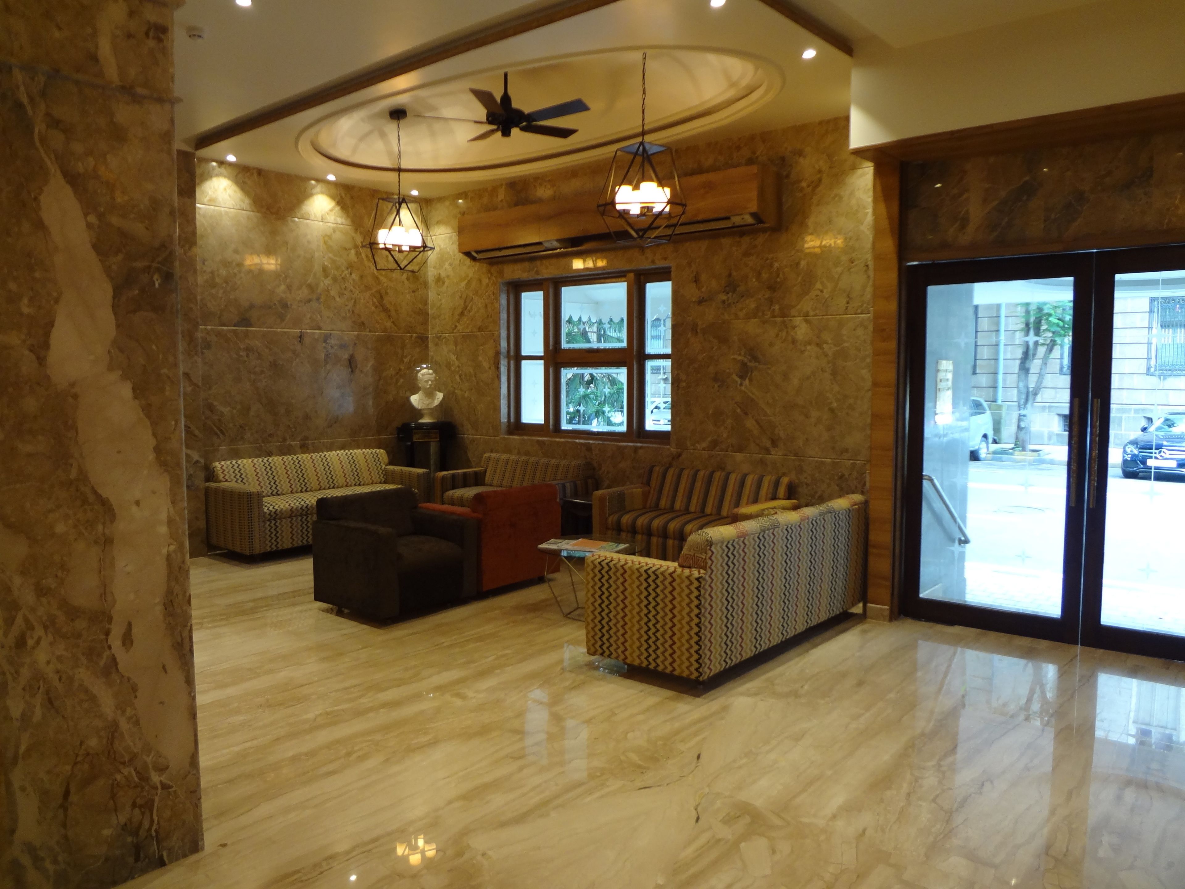 A lobby with marble flooring, patterned sofas, a ceiling fan, and large windows.