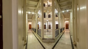 A multi-level corridor with white walls and tiled floors, featuring a central open area with a railing. - Grand Hotel, Mumbai - Ballard Estate, Fort (Mumbai)