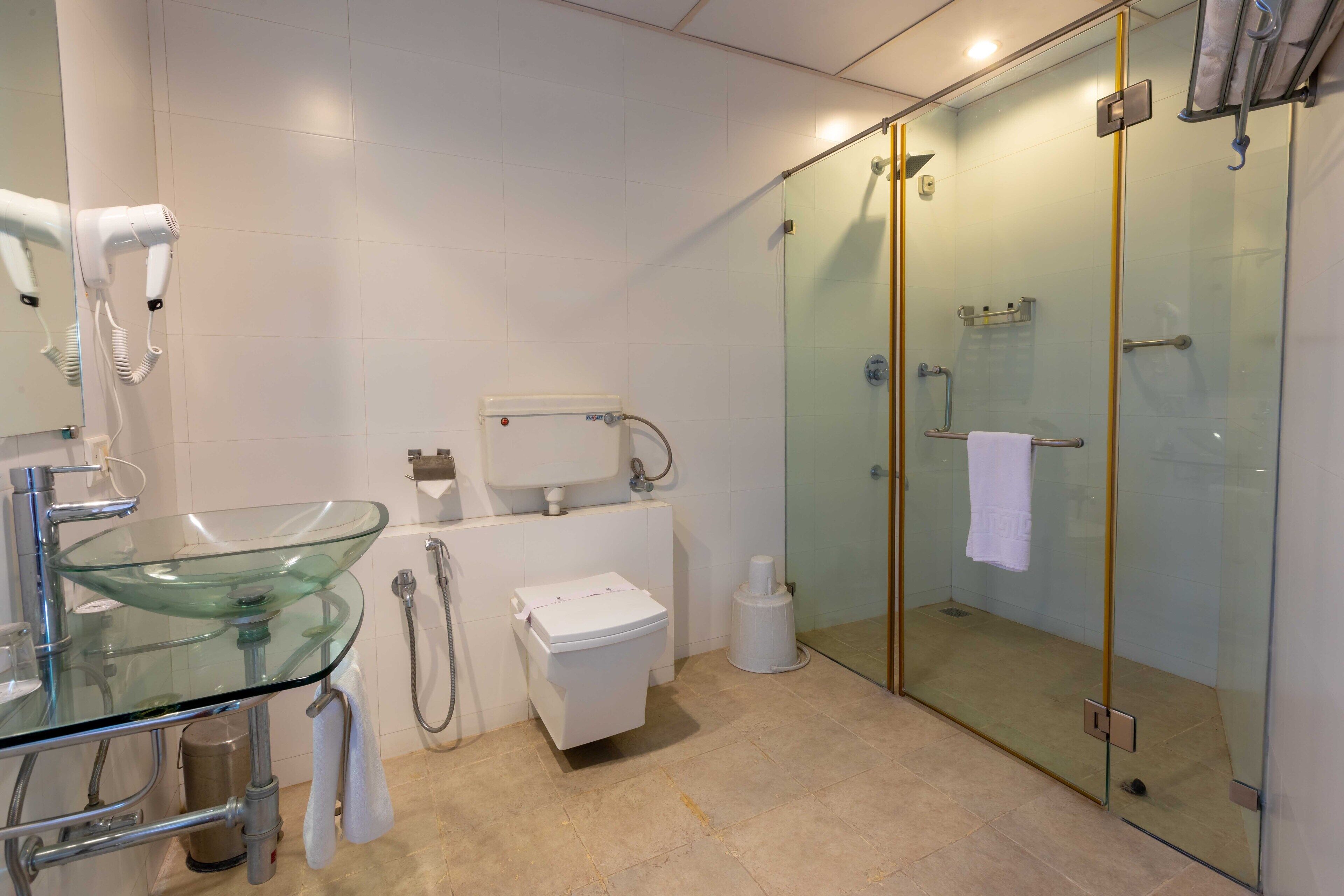 A modern bathroom with a glass sink, a toilet, and a glass-enclosed shower.
