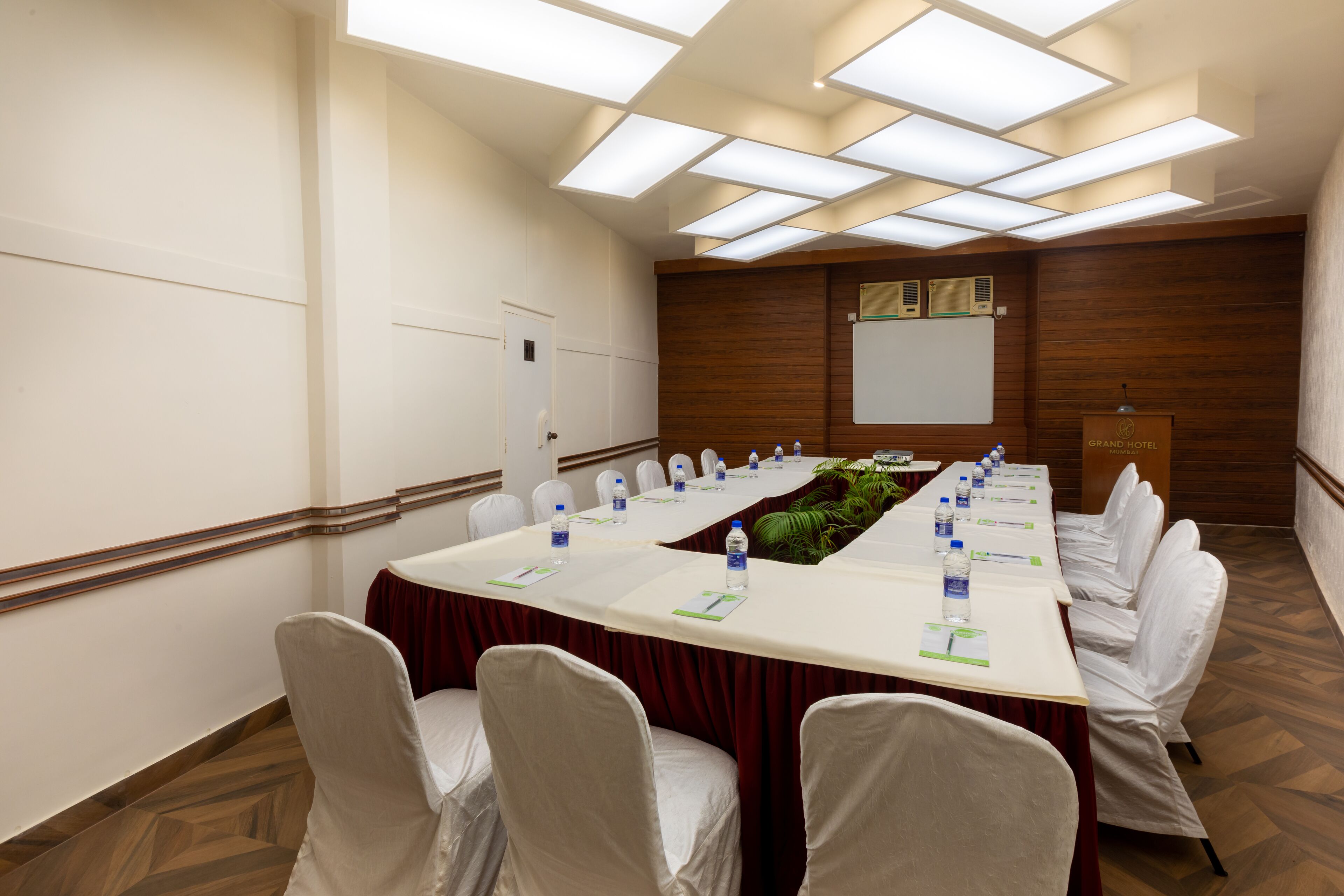 A conference room with a long table, white chairs, and a wooden panel wall.