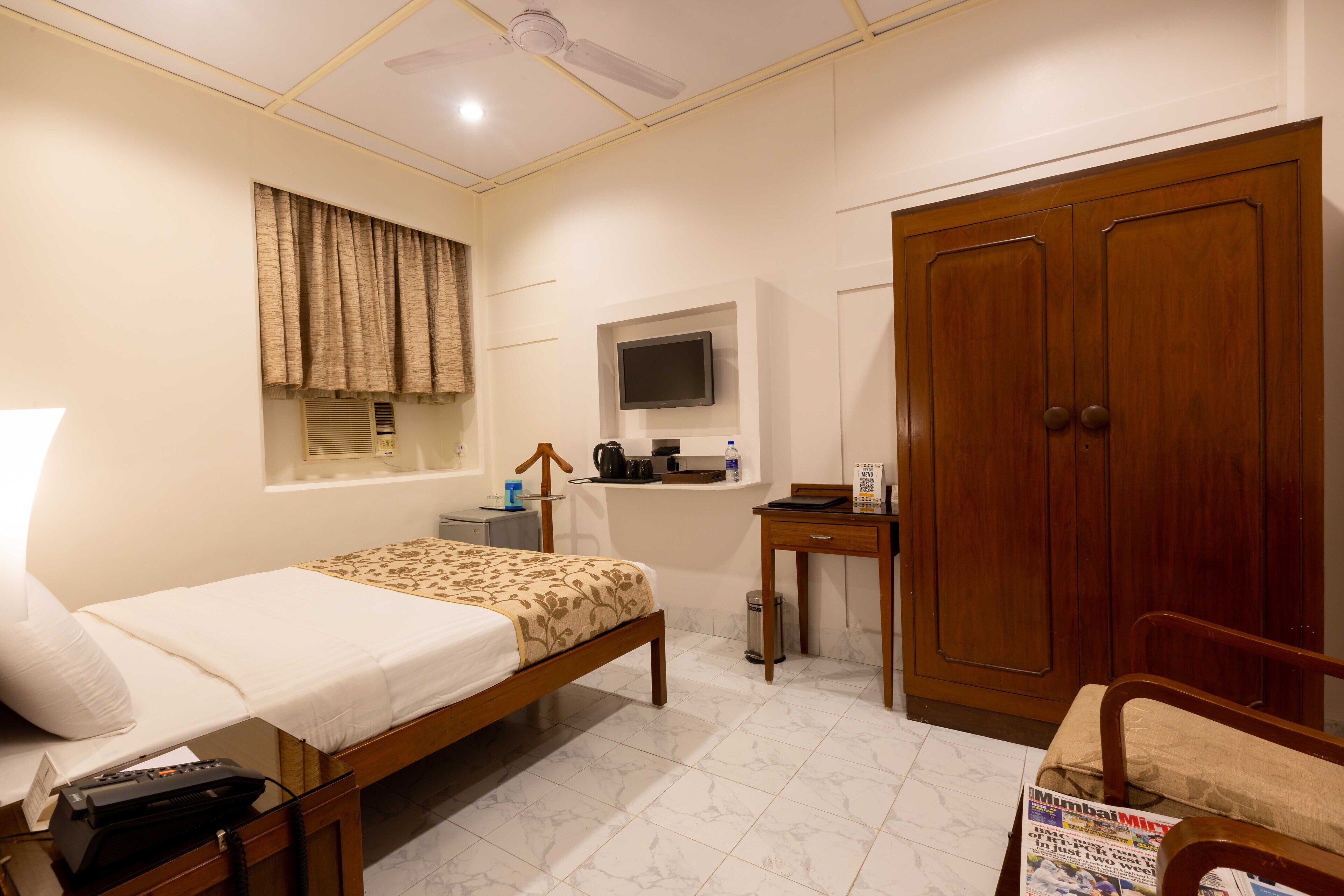 A hotel room with a bed, a desk, a wardrobe, a television, and a window with curtains.