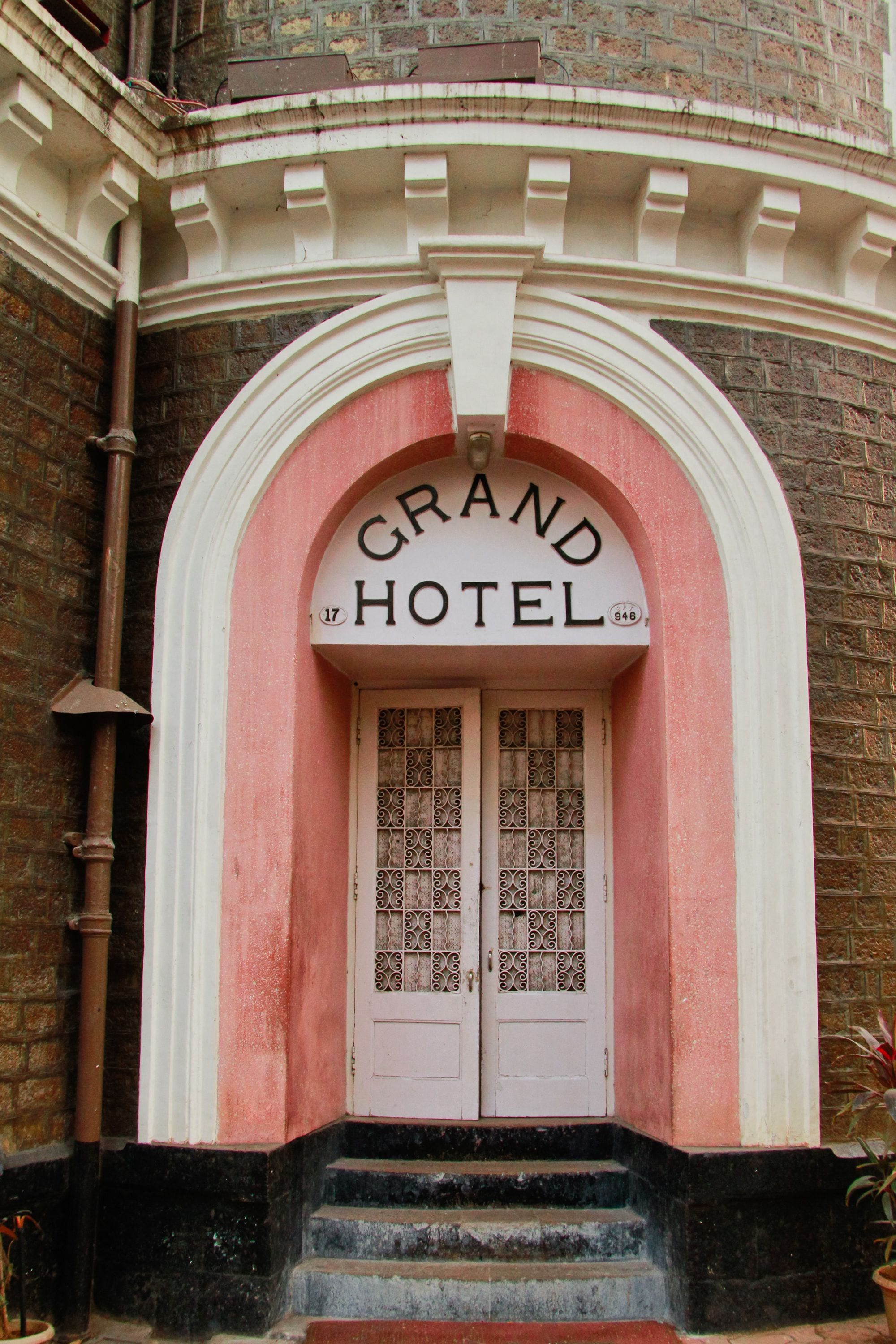 De ingang van het Grand Hotel, met een roze gevel, een witte boog en een bord boven de deur.
